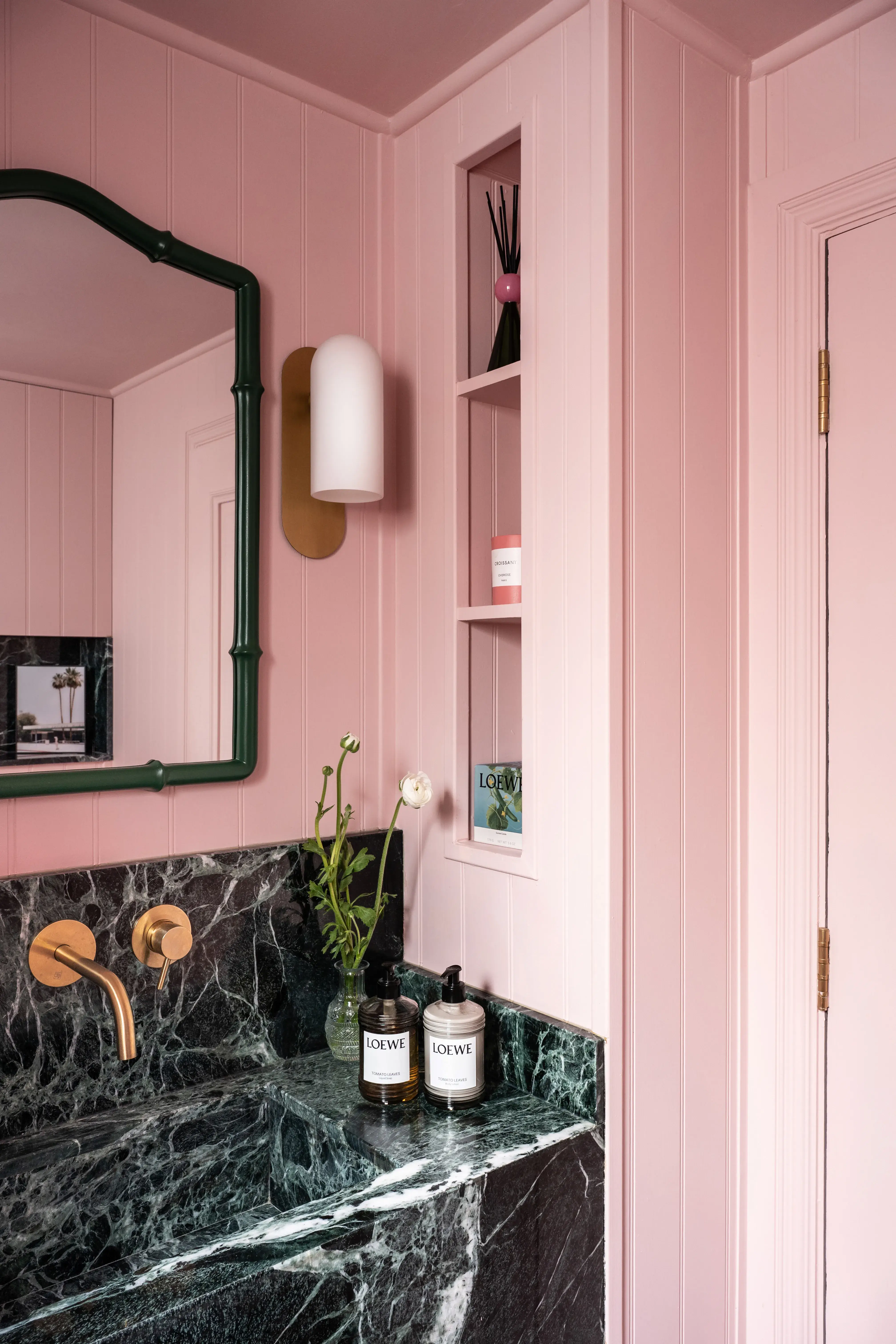 Stylish bathroom featuring pink paneling, a black marble sink, decorative shelving, and elegant fixtures.