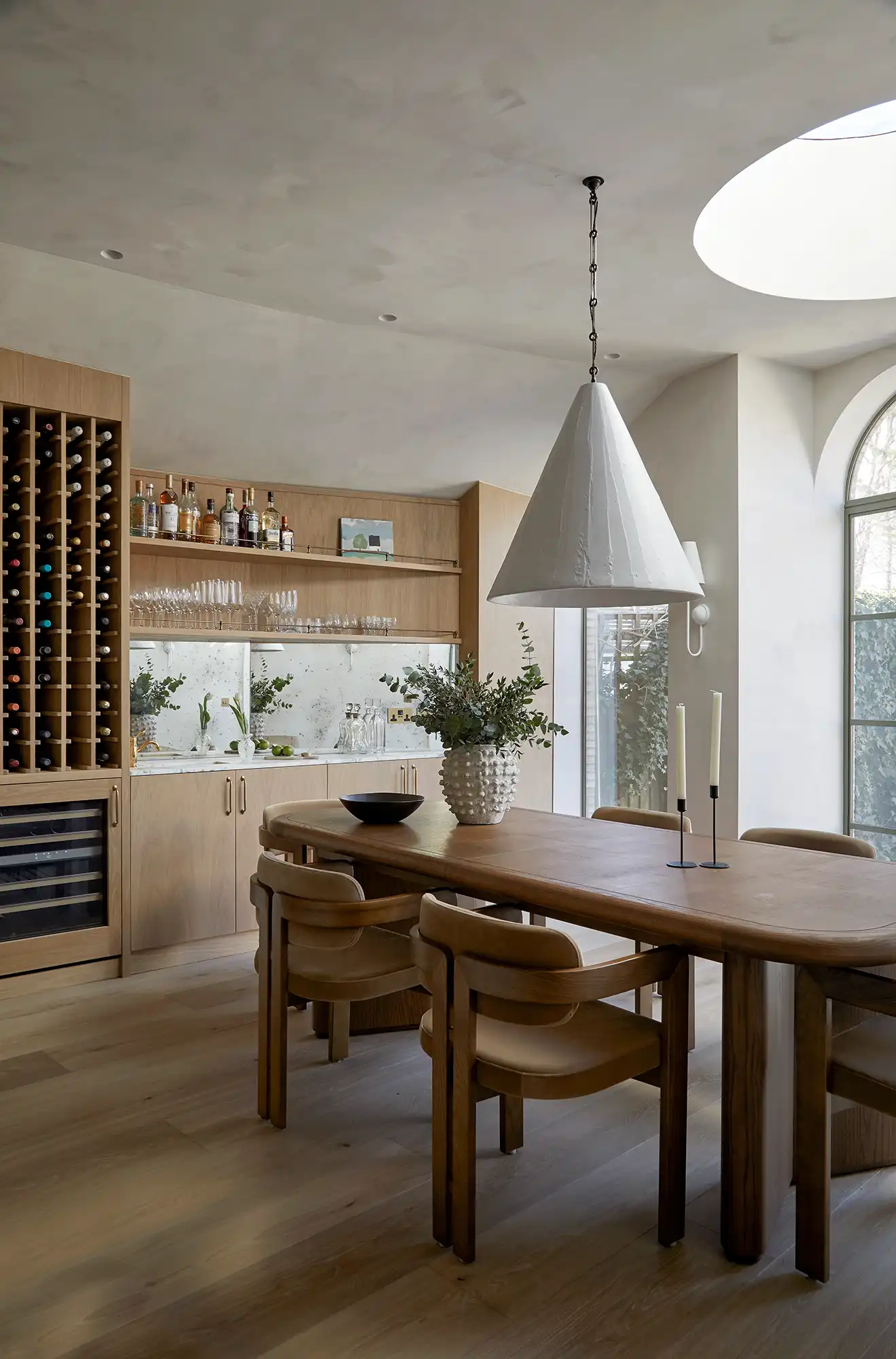 Modern kitchen-dining area featuring a wooden table, round chairs, a large pendant light, and wine storage unit.