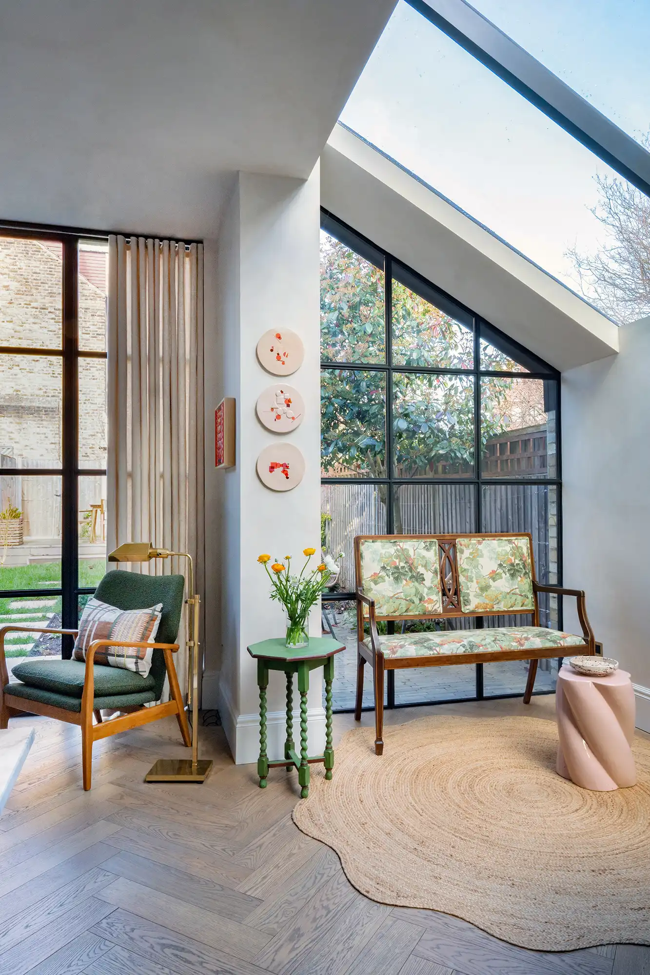 Cozy modern living space featuring a green chair, floral-bench, small green table with flowers, and large windows with natural light.